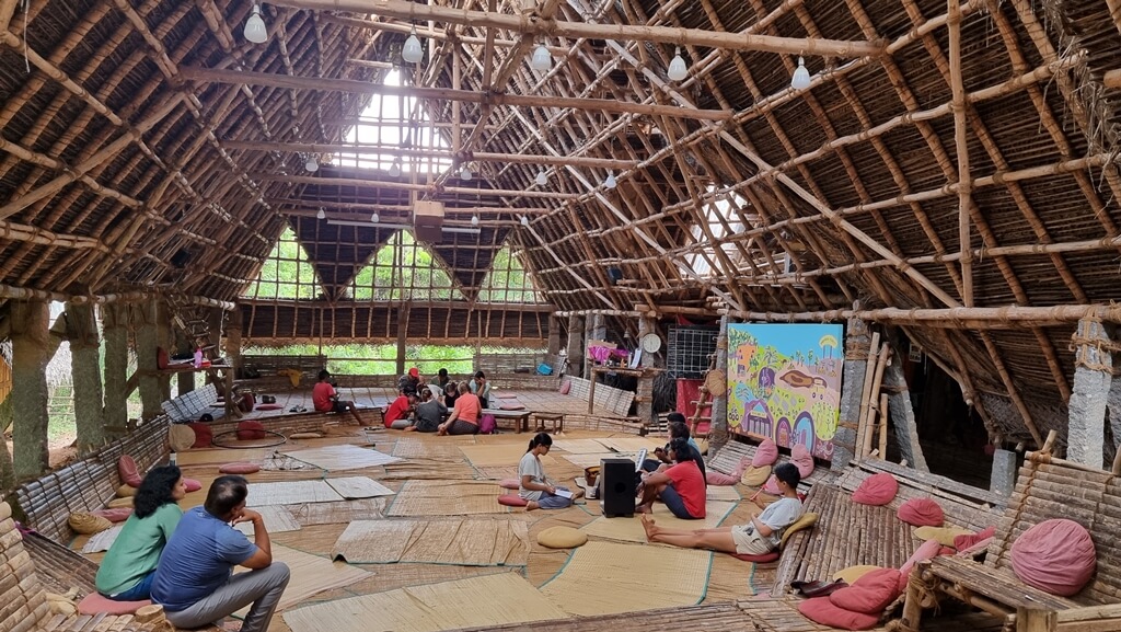 Community members living in the Sadhana forest can be seen participating in activities and discussions inside the big man-made hut 