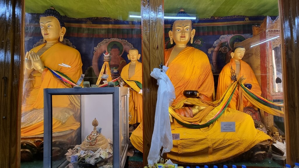 Several Bodhisattva statues on display in a mirror case with food and money offerings made by the visitors